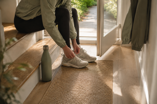 Person lacing walking shoes by an open front door in morning light