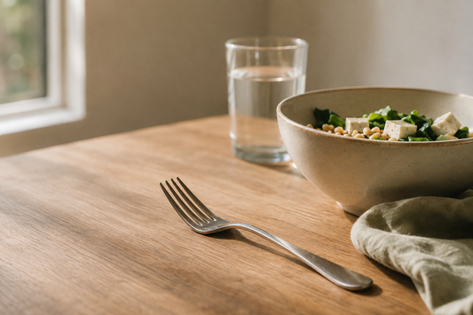 A fork set down beside a bowl of food on a bare table