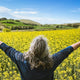 Woman embraces a field of yellow flowers.