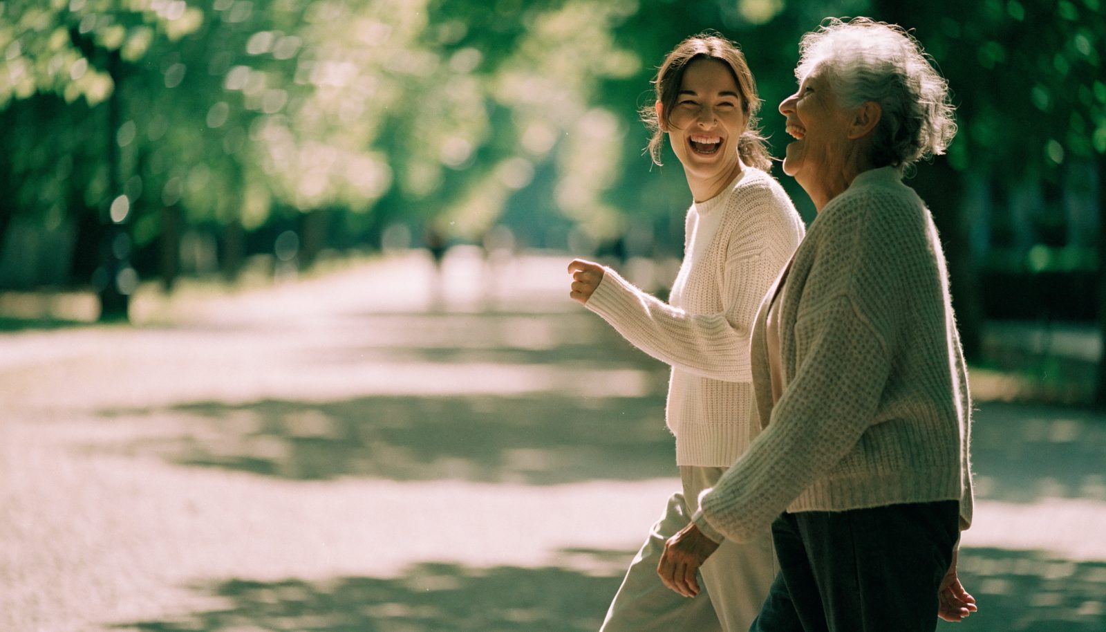 Two women walking and laughing on a sunlit path